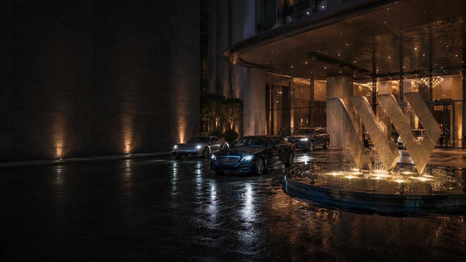 Luxury cars — a Porsche, Mercedes-Benz S-Class and Audi — at the lit entrance of a Hong Kong building at night